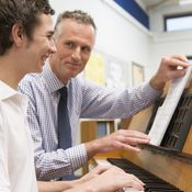 Teacher with schoolboy playing piano in music class